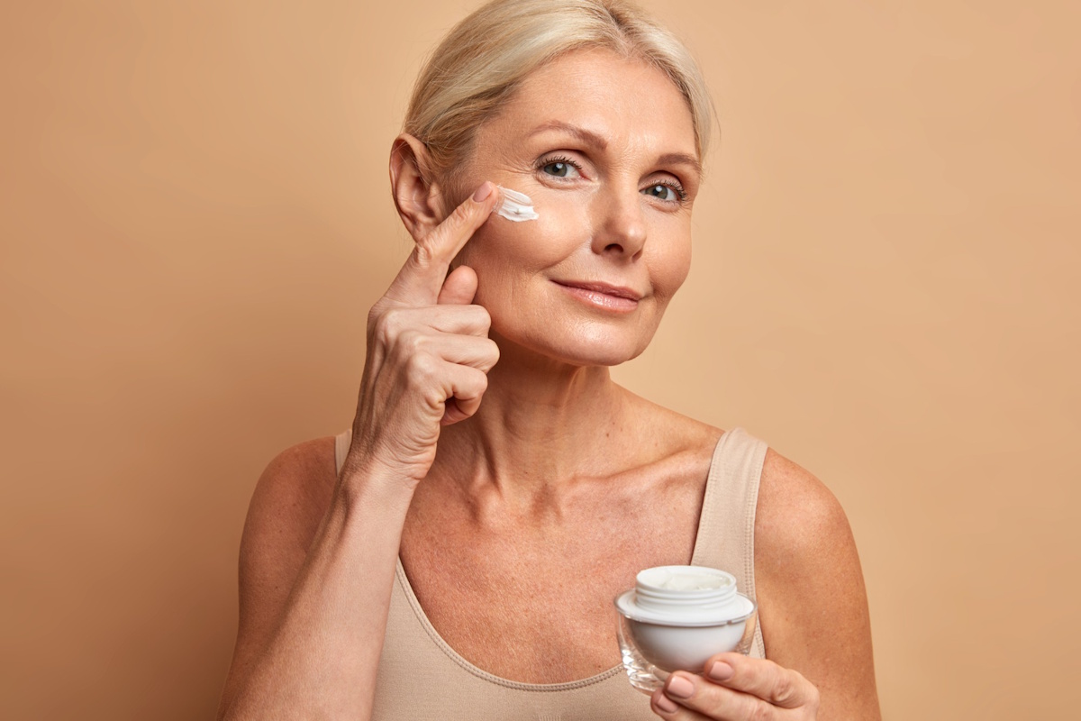 femeie aplicand crema antiaging pe fata in zona ridurilor, ingrijire ten matur menopauza