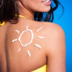 Femeie in costum de baie cu un soare desenat din crema cu protectie solara