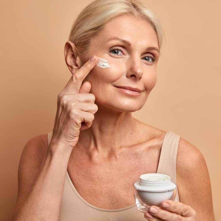 femeie aplicand crema antiaging pe fata in zona ridurilor, ingrijire ten matur menopauza